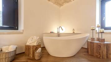 Une salle de bain moderne avec une baignoire sur pieds, des tables d’appoint en bois et une fenêtre laissant entrer la lumière naturelle.