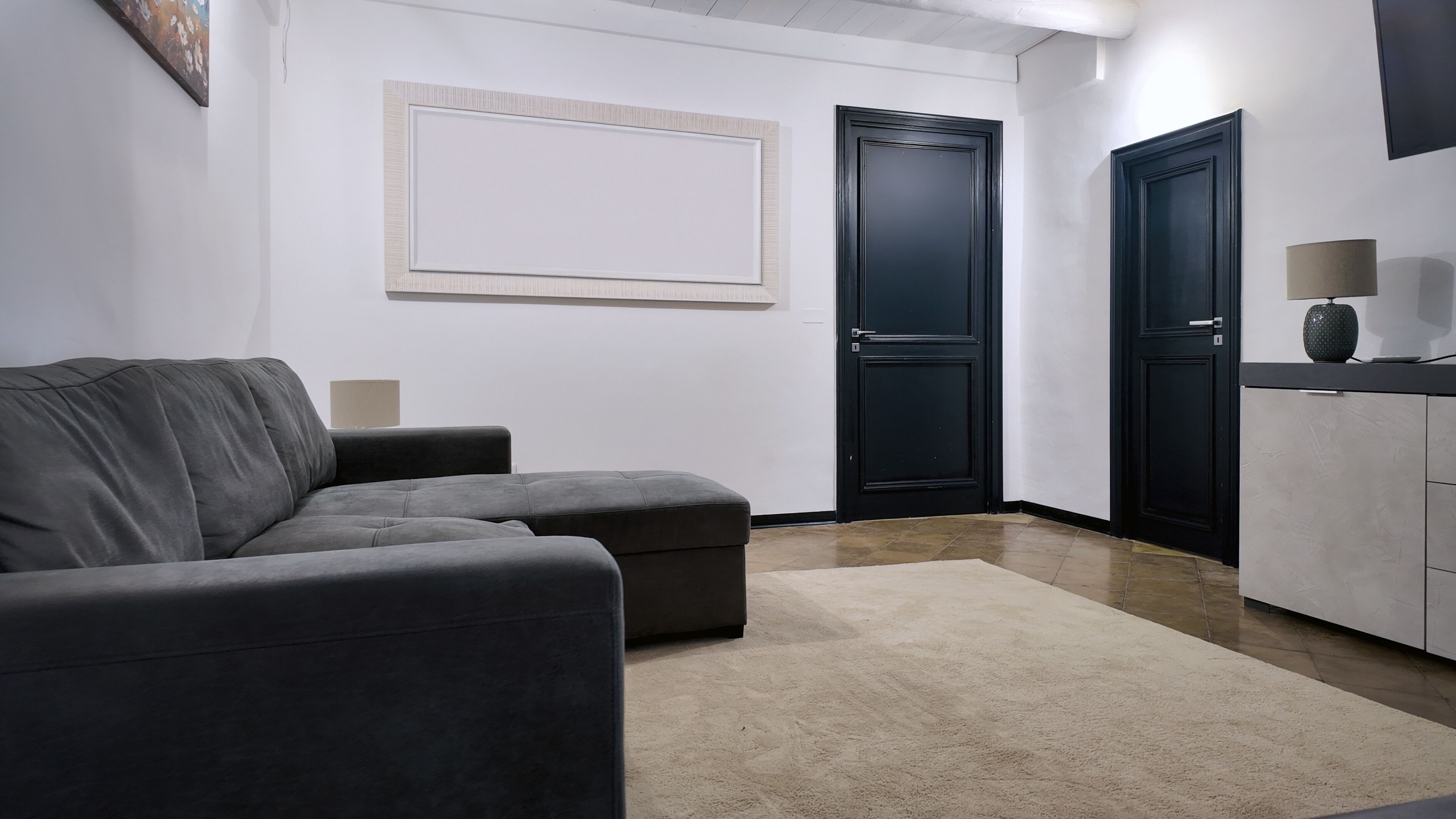 A modern living room with a grey sofa, a beige rug, and a black cabinet with a lamp on top.