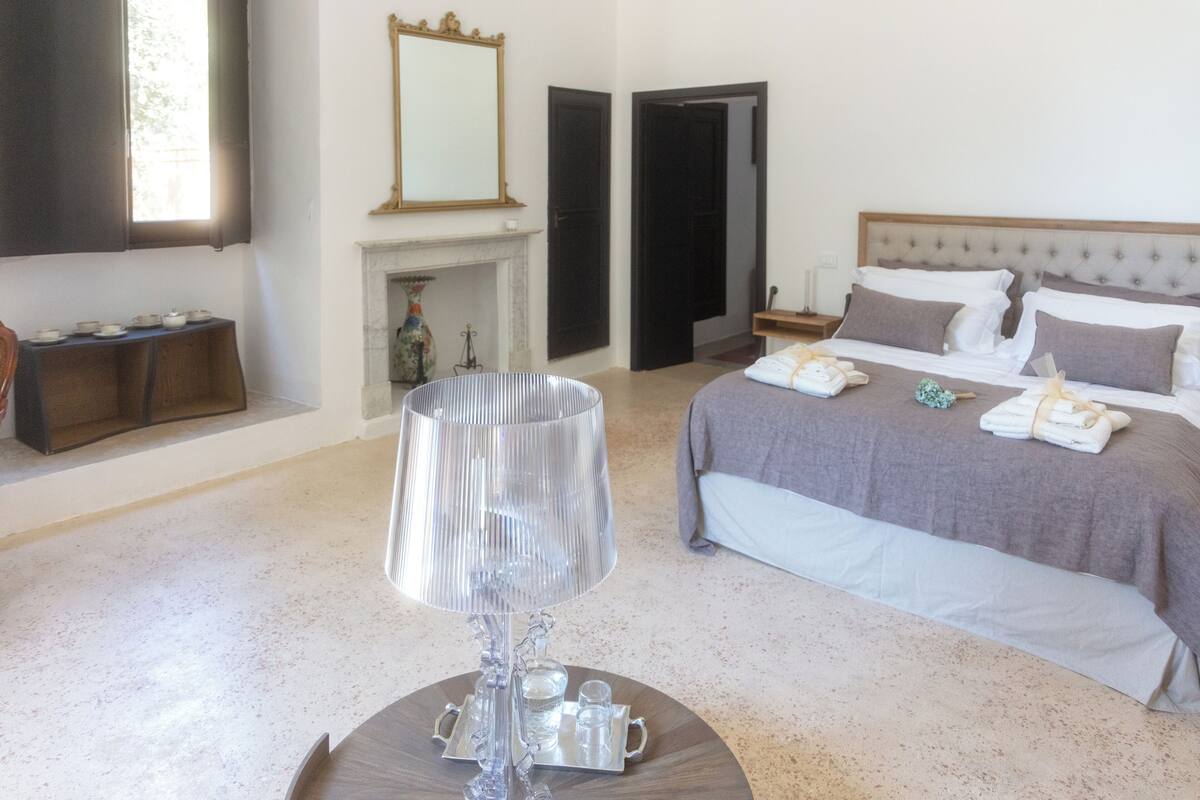 Une chambre à coucher avec un lit, des tables de chevet, une lampe et une cheminée.