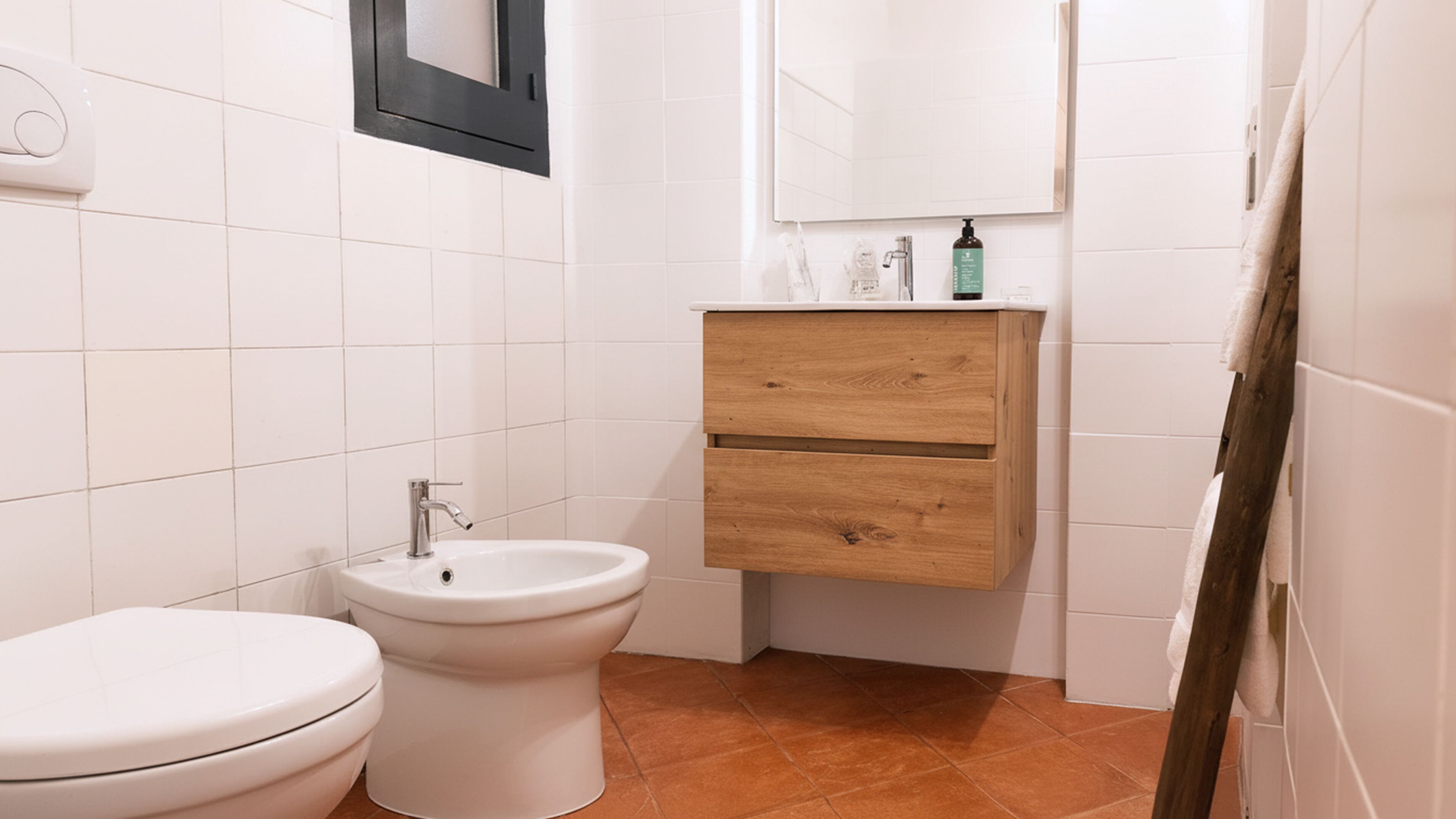 Une salle de bain équipée de toilettes, d’un bidet et d’un meuble-lavabo en bois avec un miroir et des articles de toilette.