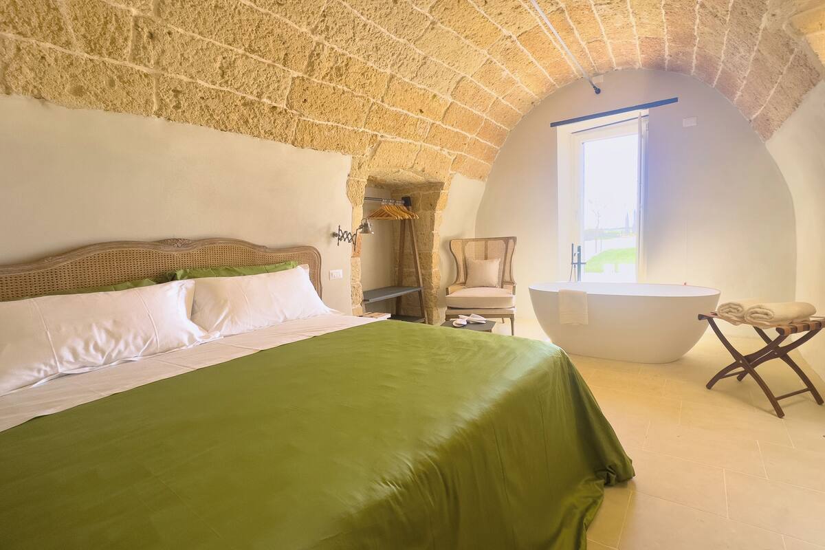 Une chambre avec un grand lit, une chaise, une baignoire et une fenêtre.