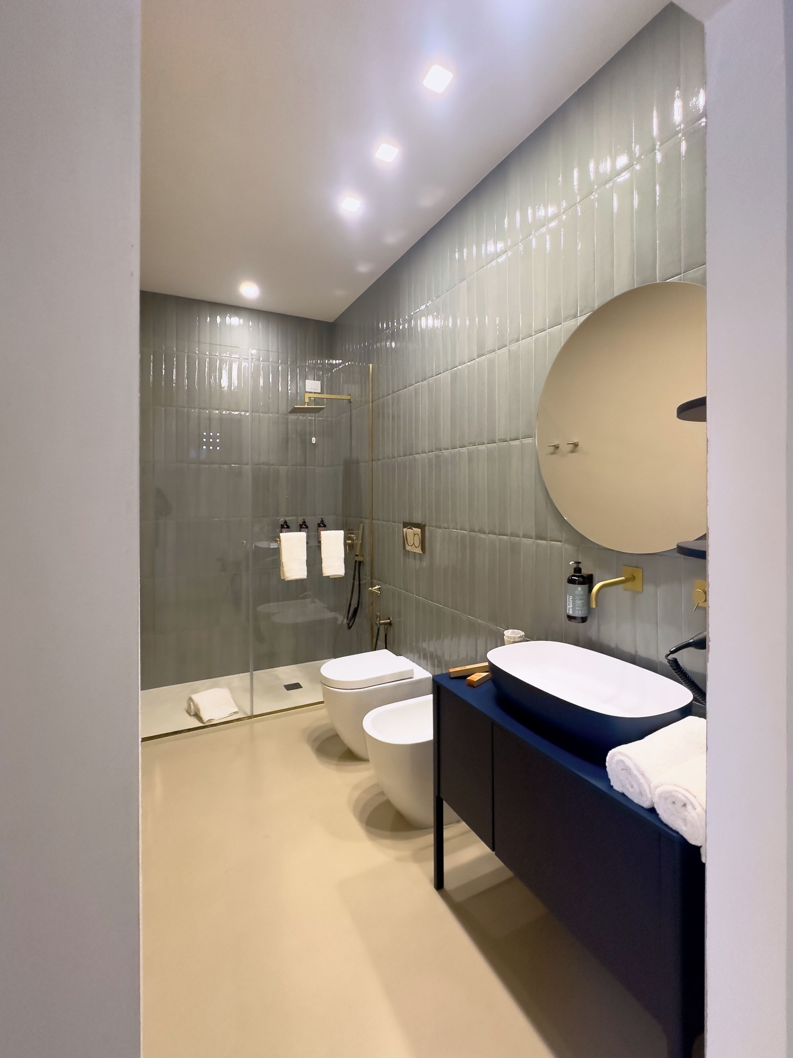 Une salle de bain moderne dotée d’une douche à parois de verre, de deux toilettes, d’un lavabo avec un grand miroir et d’un porte-serviettes.