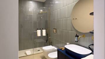 Une salle de bain moderne dotée d’une douche à parois de verre, de deux toilettes, d’un lavabo avec un grand miroir et d’un porte-serviettes.