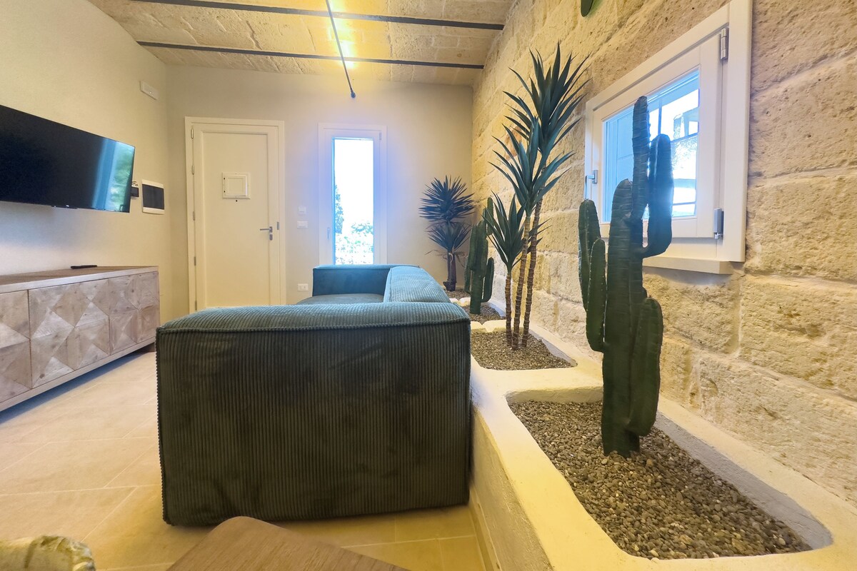 Un salon moderne avec un grand canapé d’angle, un téléviseur à écran plat fixé au mur et un mur en pierre agrémenté d’une fenêtre.