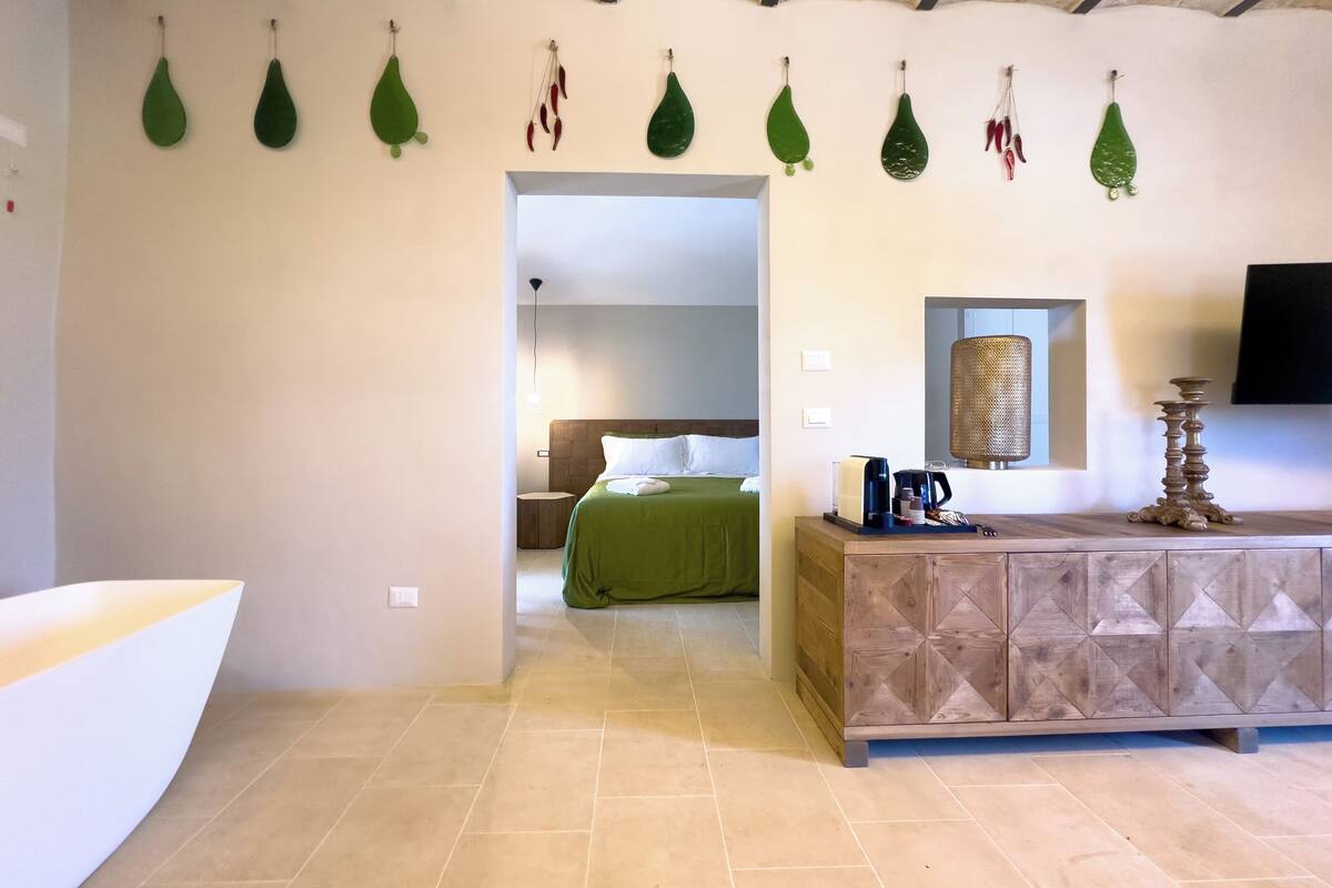 Une chambre d’hôtel avec un plafond en bois, un lit vert, une armoire en bois équipée d’un téléviseur à écran plat et un luminaire fixé au mur.