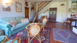 A living room with a sofa, wicker chairs, a patterned rug, and a staircase leading to another room.