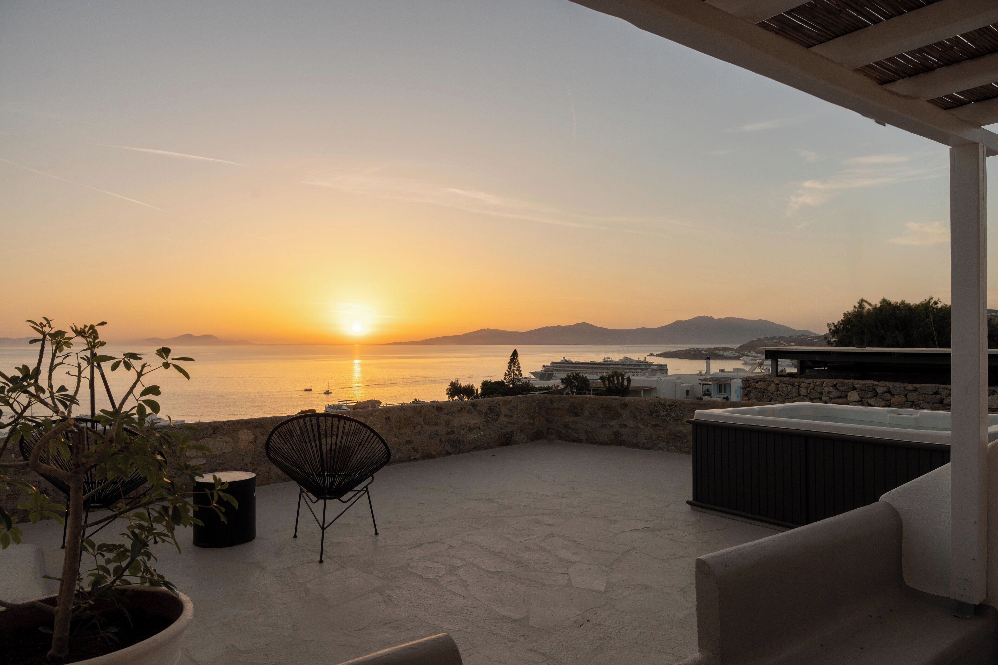 A terrace with a view of the sunset over the sea, stone flooring, and outdoor furniture.