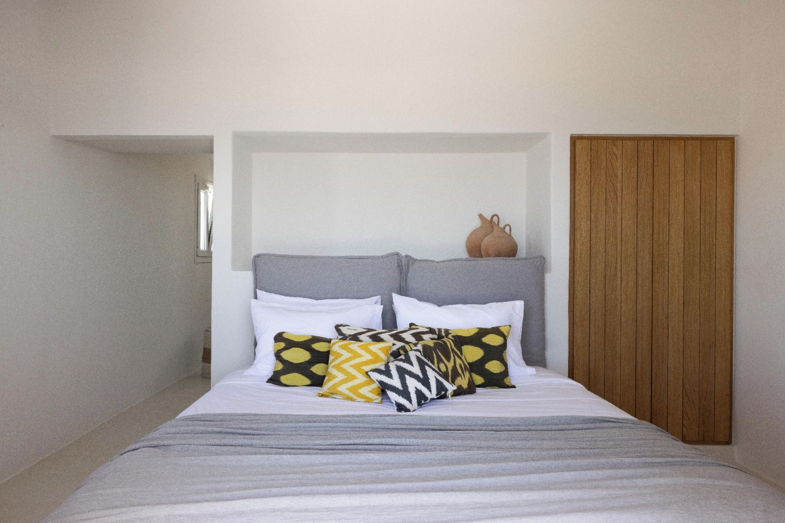 Un dormitorio con cama, almohadas, cabecera y una puerta de madera.