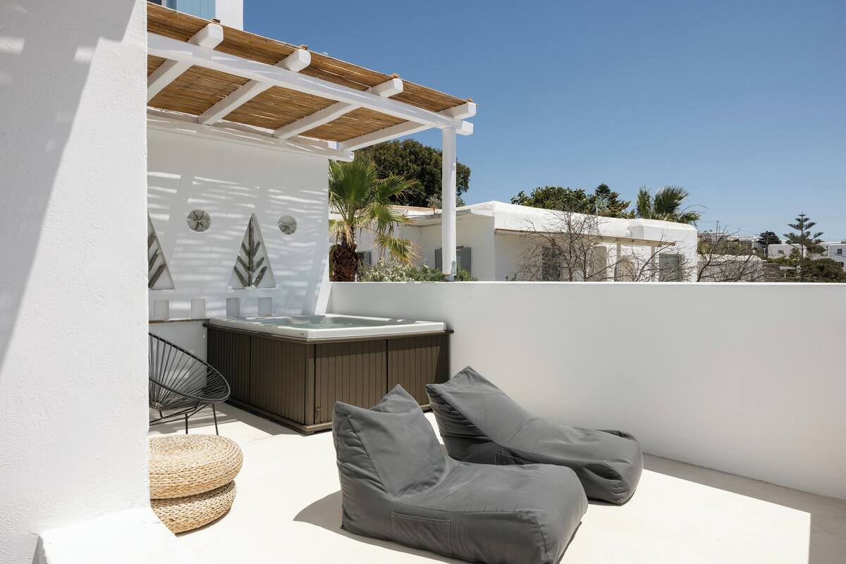 Una terraza en la azotea con un jacuzzi, sillones grises y una pérgola.