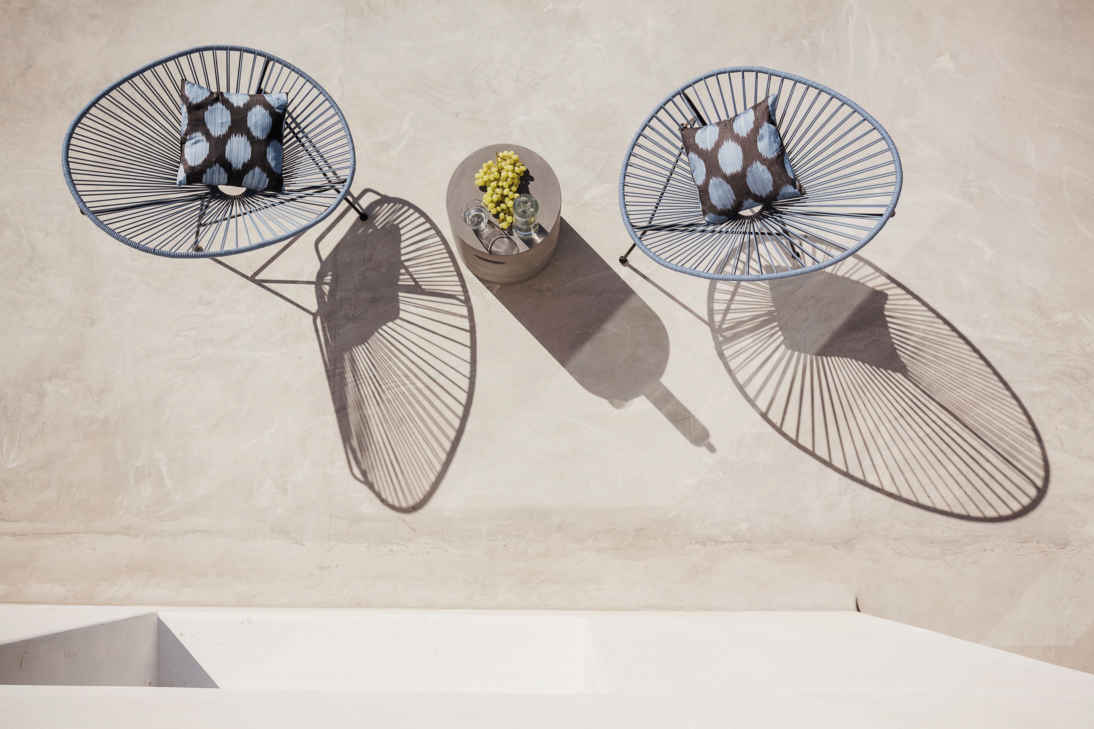 Three wire-framed chairs with cushions against a plain wall.
