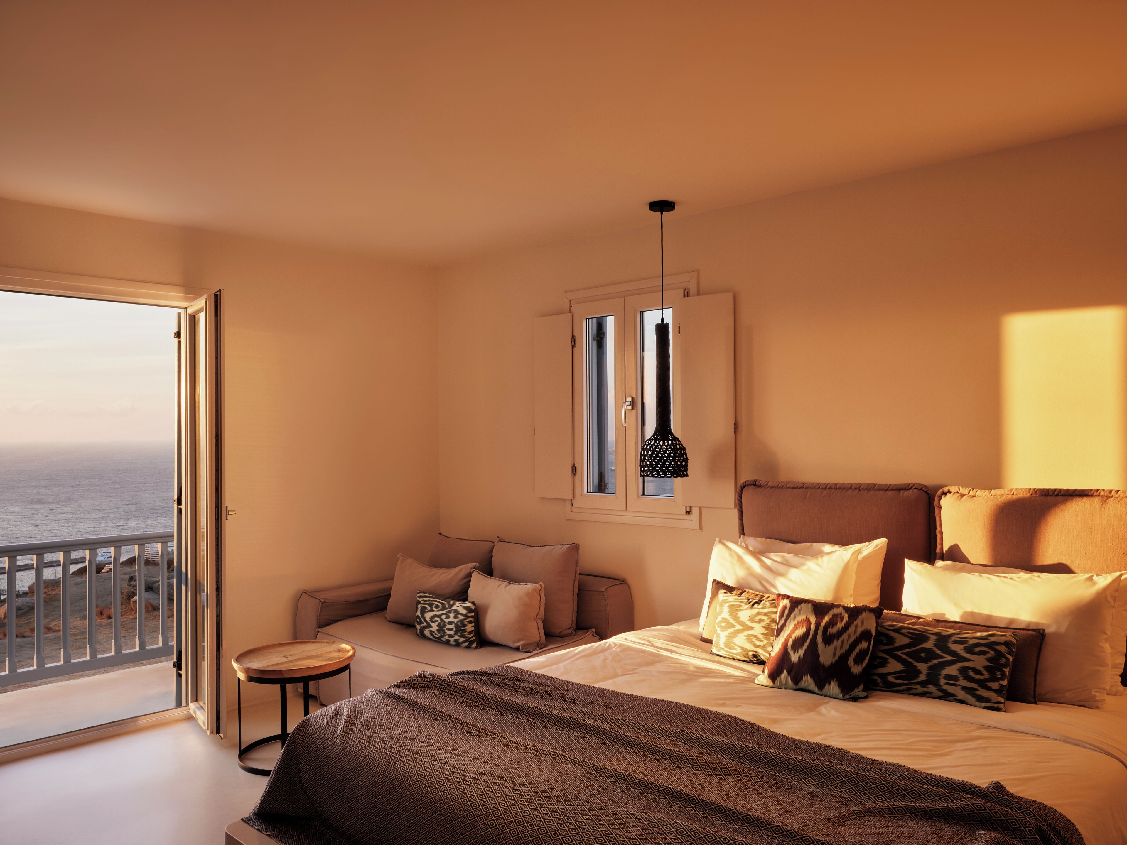 A bedroom with a large bed, a small table, a sofa, and a window with a view of the sea.