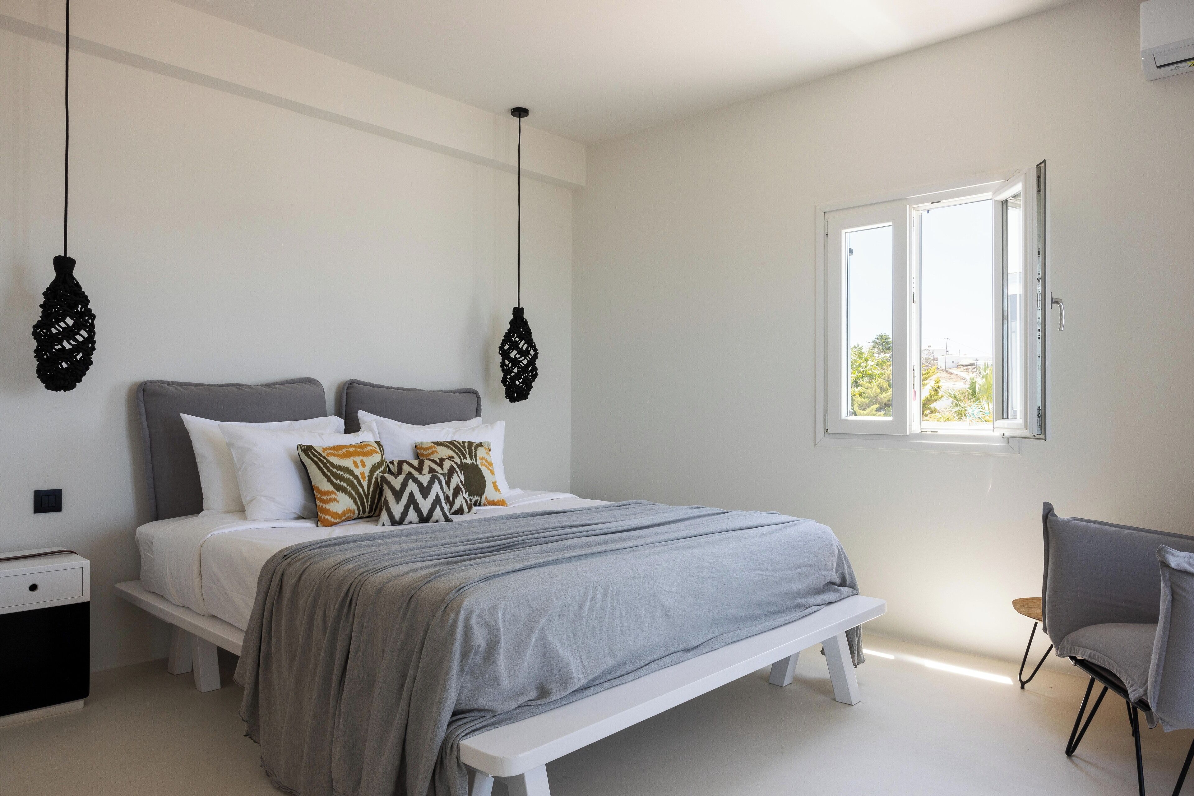 Un dormitorio moderno con una cama grande, mesitas de noche, un banco y una ventana con vistas.