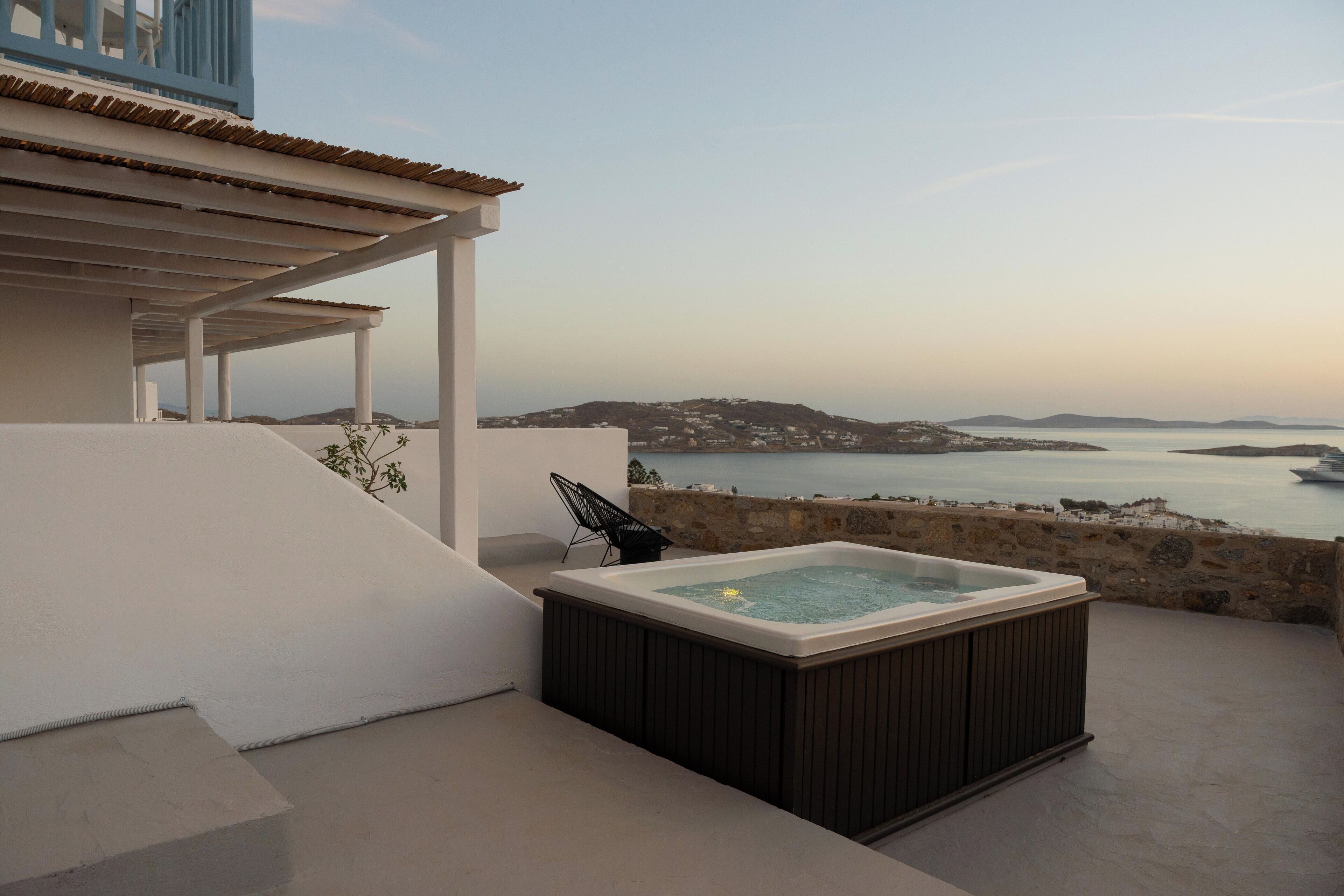 A rooftop terrace with a hot tub, a stone wall, and a view of the sea and distant hills.