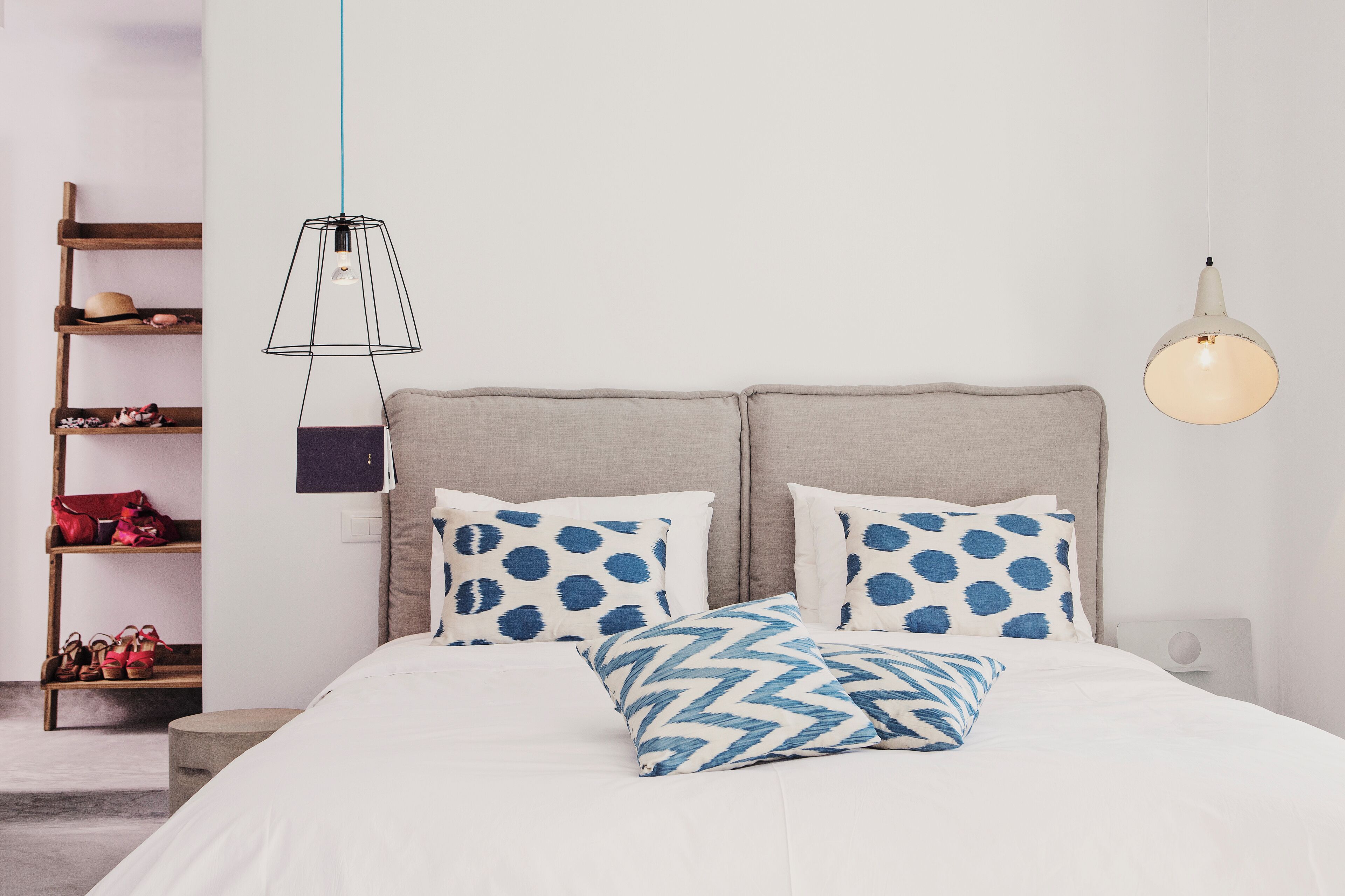 A neatly arranged bedroom with a bed, pillows, a hanging light fixture, and a wooden shelf with shoes.
