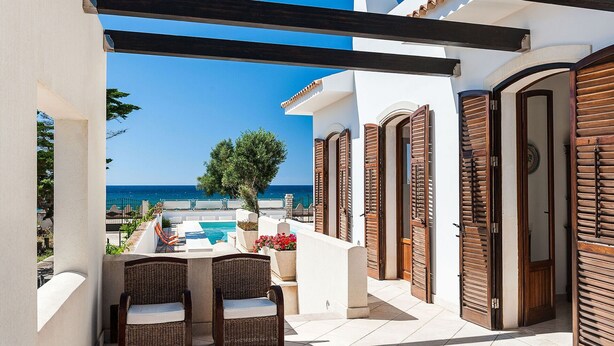 Un balcon avec des fauteuils en osier, une piscine et une vue sur la mer.
