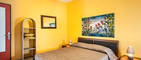 A bedroom with a bed, a nightstand, a lamp, a shelf, and a painting on the wall.