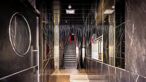 Un moderno vestíbulo de hotel con piso de mármol, una escalera que conduce a una zona iluminada en rojo y una cámara de seguridad en el techo.