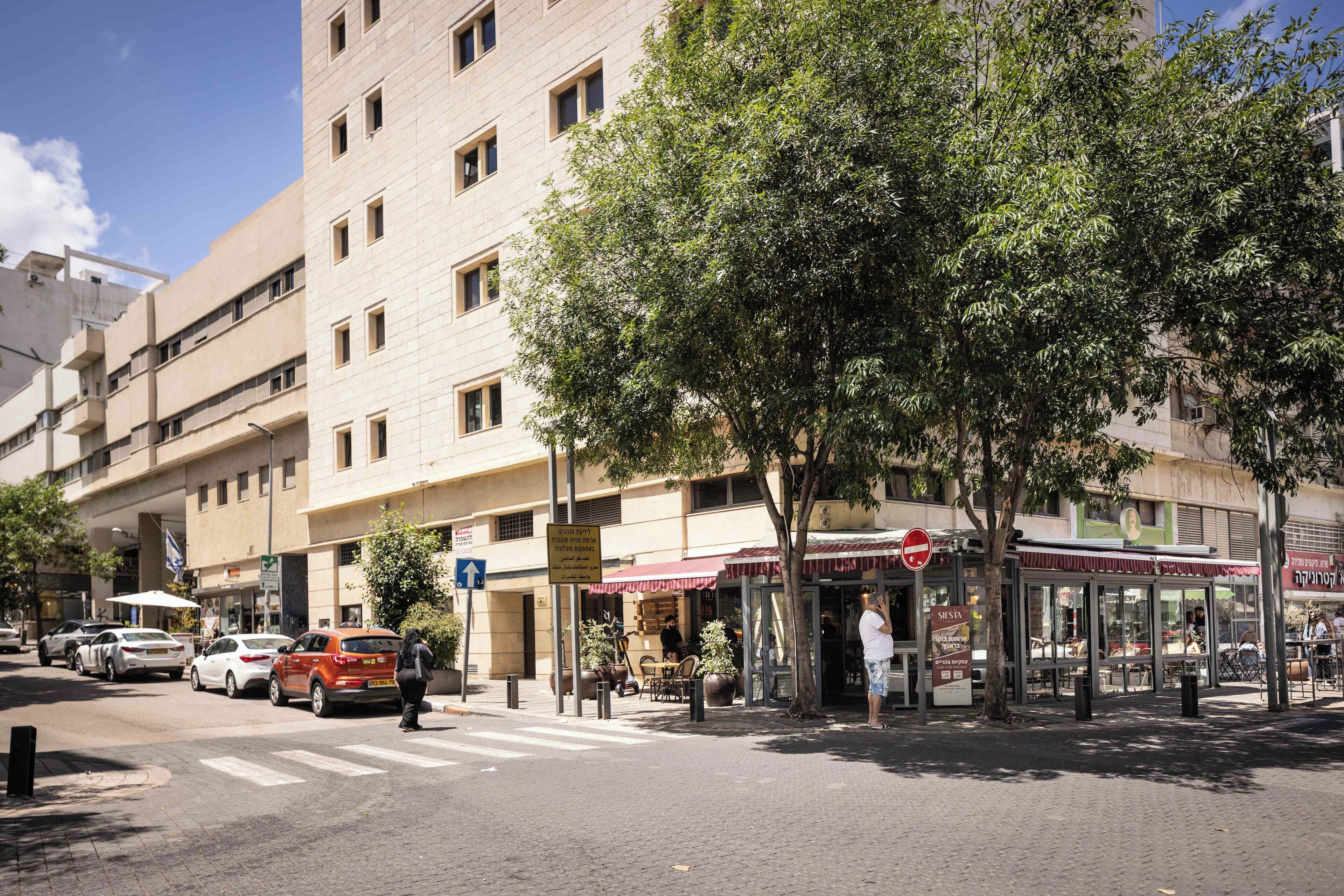 Una vista di strada con un edificio su più piani, un attraversamento pedonale e un caffè con tavolini all'aperto.