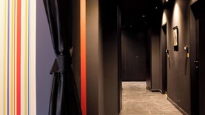 Un pasillo con paredes oscuras y piso de baldosas, que conduce a una puerta con un pequeño cuadro enmarcado en la pared.