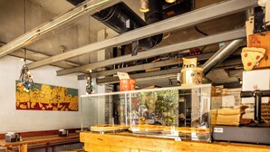 Interior de restaurante con bancos de madera, una exposición de pizzas y un mural en la pared.
