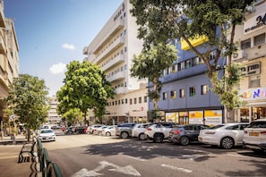Vista de una calle con coches aparcados, árboles y edificios con señalización.