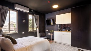 Una habitación de hotel moderna con una cama grande, un escritorio pequeño, un televisor y una kitchenette.