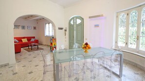 A dining area with a glass table and chairs, a red sofa, and a fruit bowl.