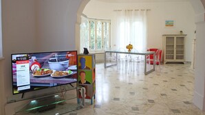 A modern interior with a dining area, a TV displaying a food advertisement, and a clear view of the kitchen in the background.
