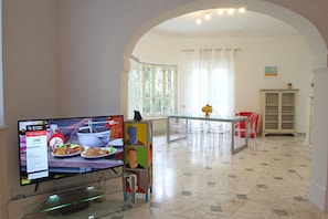 A modern interior with a dining area, a TV displaying a food advertisement, and a clear view of the kitchen in the background. - Stunning private villa with A/C, WIFI, TV, veranda and pets allowed, close to Forte Dei Marmi (Marina Dei Ronchi)