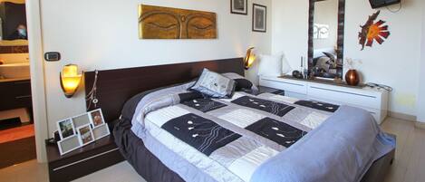 Un dormitorio con una cama grande, una mesita de noche, un aparador, un espejo y decoración en la pared.
