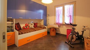 A bedroom with a bed, storage cabinets, a window with curtains, a bicycle, and a trash bin.