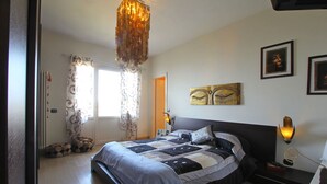 A bedroom with a bed, a chandelier, a bedside table with a lamp, and artwork on the wall.