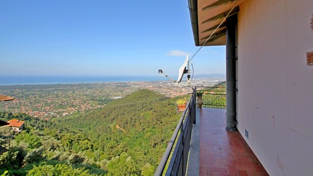 A balcony with a view of a coastal city, a satellite dish, and a potted plant.
