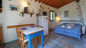 A compact room with a dining table, chairs, a bed with a blue patterned bedspread, a refrigerator, and a wooden ceiling. - Beautiful private villa for 3 guests with A/C, hot tub, TV, veranda, pets allowed and panoramic ... (Castiglione Della Pescaia)