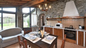 Una cocina rústica con paredes de piedra, vigas de madera y un comedor con una mesa preparada para dos.
