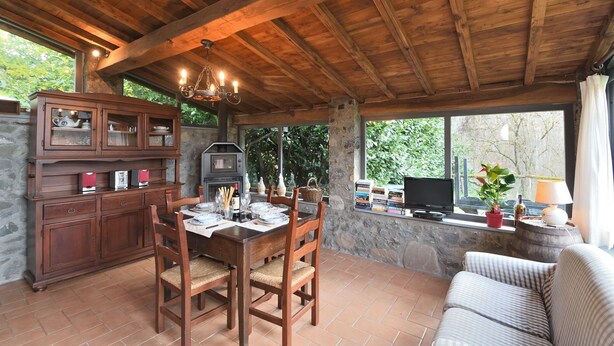 Un comedor rústico con techo de madera, paredes de piedra y vista a la vegetación.