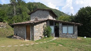 Una cabaña de piedra con puerta de madera, un pequeño porche y una ventana con cortinas.