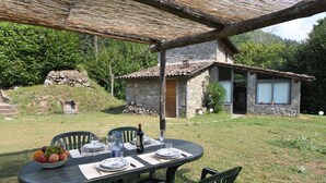 Un área de comedor al aire libre con una mesa preparada para dos, rodeada de muros de piedra y una casa de piedra al fondo.
