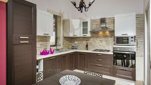 A modern kitchen with dark wooden cabinets, a white countertop, a gas stove, a microwave, and a chandelier. - Beautiful private villa for 8 guests with private pool, WIFI, A/C, TV, veranda and panoramic view (Castellammare Del Golfo)