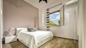 A bedroom with a bed, nightstand, lamp, and a window with a view of a hill. - Beautiful private villa for 8 guests with private pool, WIFI, A/C, TV, veranda and panoramic view (Castellammare Del Golfo)