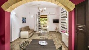 A modern living room with a sofa, dining table, and chairs. There is a TV mounted on the wall and a window with a view of greenery. - Beautiful private villa for 8 guests with private pool, WIFI, A/C, TV, veranda and panoramic view (Castellammare Del Golfo)