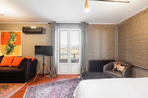 A hotel room with a bed, a sofa, a chair, a television, and a view of the outdoors through a glass door. - Milea Agritourism (Tripoli)