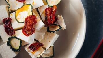 Un tazón de cubos de tofu con tomates secos al sol sobre una superficie oscura.
