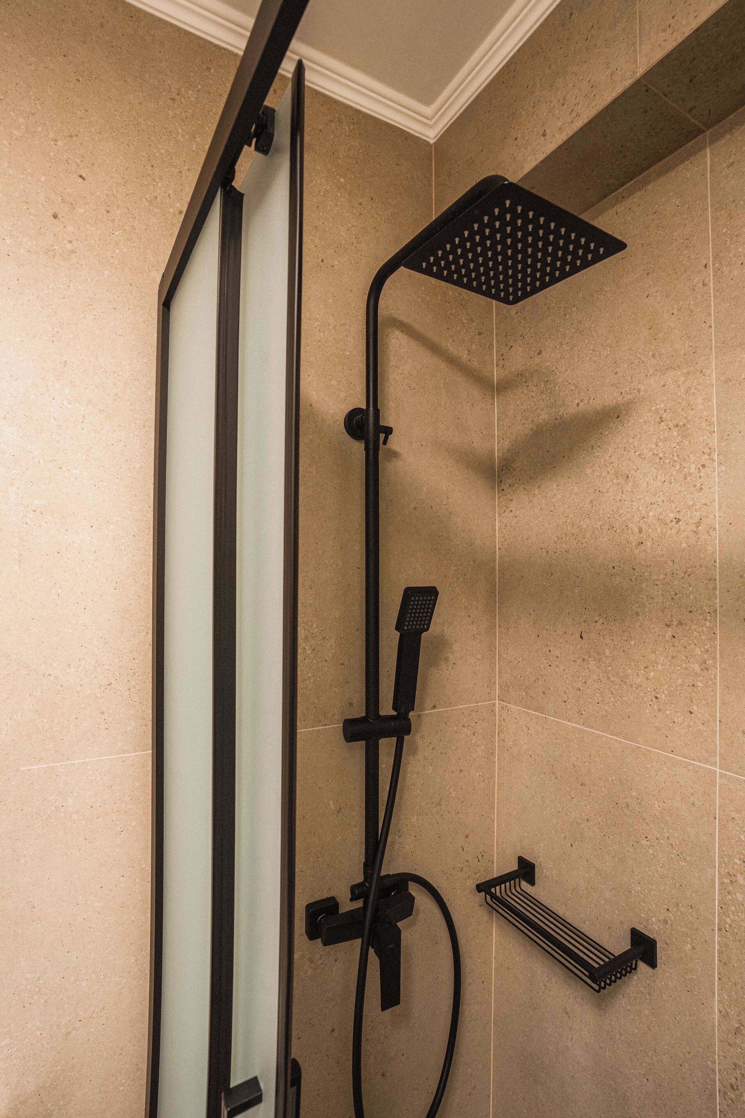 A shower with a glass door, a handheld showerhead, and a towel rack.