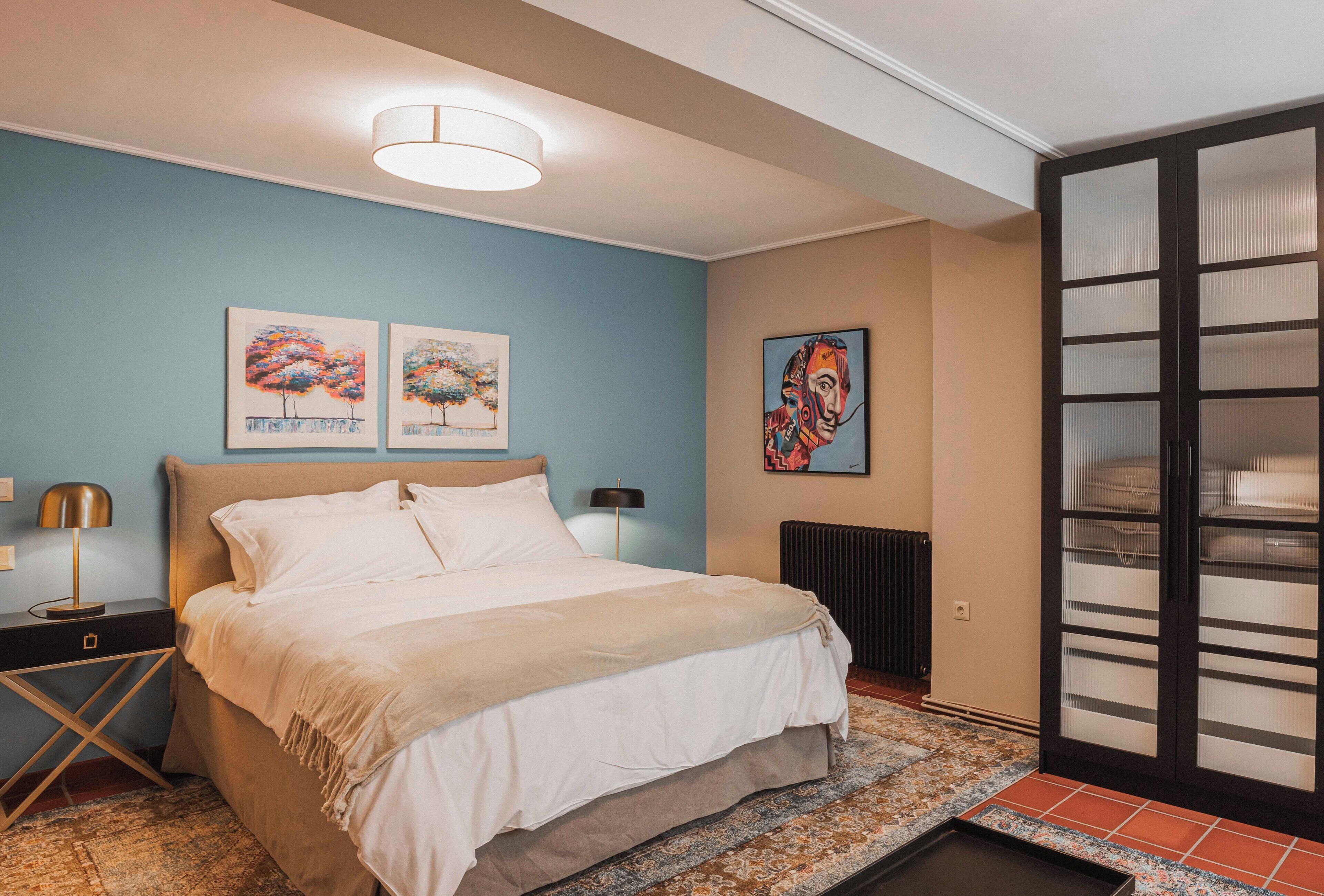 A bedroom with a bed, two wall art pieces, a nightstand, a lamp, and a sliding door with a view.