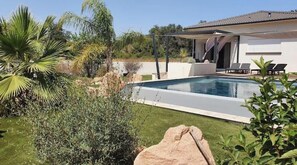 Ett modernt hus med en swimmingpool, omgivet av frodig grönska och palmer.