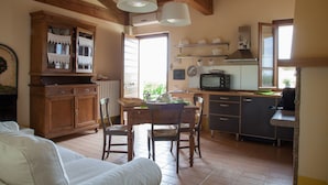 A cozy kitchen with wooden cabinets, a dining table with chairs, and a built-in microwave. - Cosy apartment for 3 people with WIFI, pool, A/C, TV and pets allowed (Isola Di Fano)