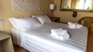 A neatly made bed with white linens and two rolled towels, a bedside lamp, a chair, and a mirror on the wall. - Cosy apartment for 3 people with WIFI, pool, A/C, TV and pets allowed (Isola Di Fano)