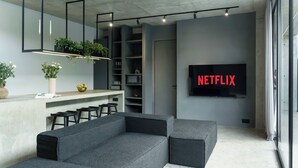 En moderne stue med en grå hjørnesofa, et barområde med barstole, et fladskærms-tv og indbyggede reoler.