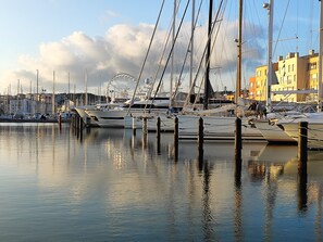 A marina with boats docked, a Ferris wheel in the background, and buildings along the waterfront.